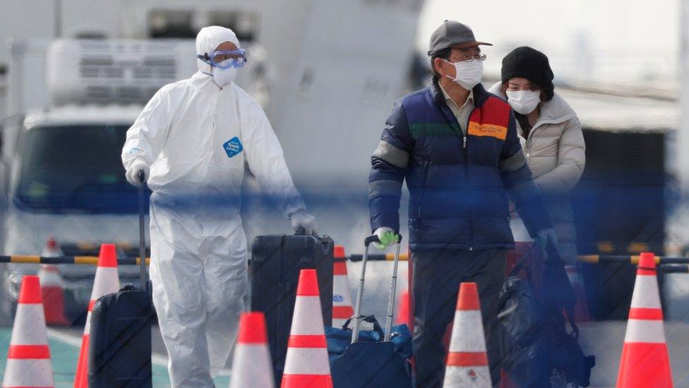 Workers in protective gear escort disembarking passengers to a vehicle from the Diamond Princess cruise ship