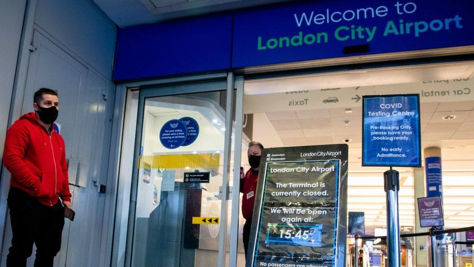 A man wearing a mask stands outside London City Airport