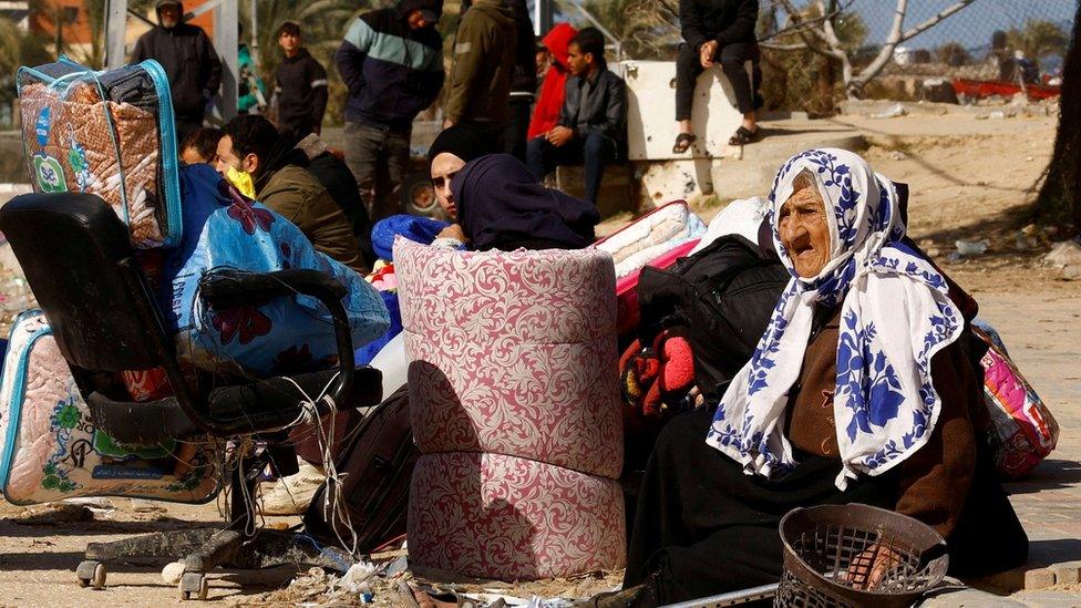 Displaced Palestinians rest on a roadside after fleeing the city of Khan Younis, in the southern Gaza Strip (30 January 2024)