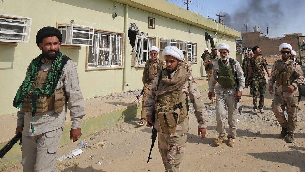 Shia fighters from the paramilitary Popular Mobilisation force walk inside al-Nour district of Tal Afar, northern Iraq (23 August 2017)