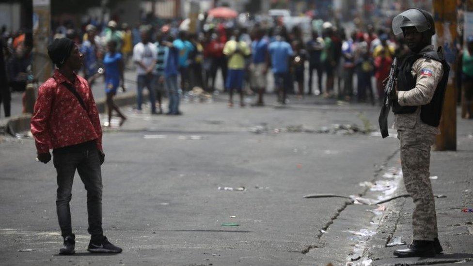 A man talks to a Haitian National Police officer guarding a commercial area that was looted during protests against fuel price increases in Port-au-Prince, Haiti, July 8, 2018.