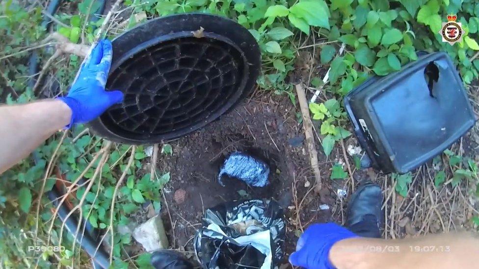 A bag of cocaine hidden under ground, covered by a bin lid