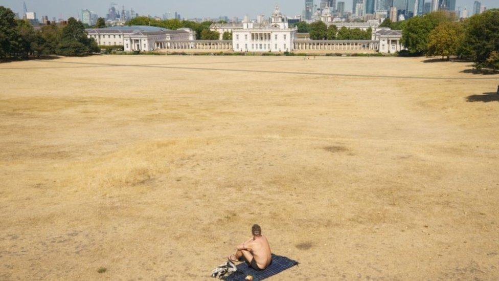 A man sits on the dry, yellow grass as the heat continues