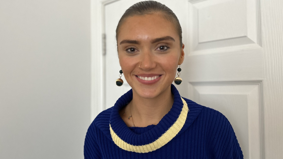 Woman in a blue jumper in front of a white internal door.