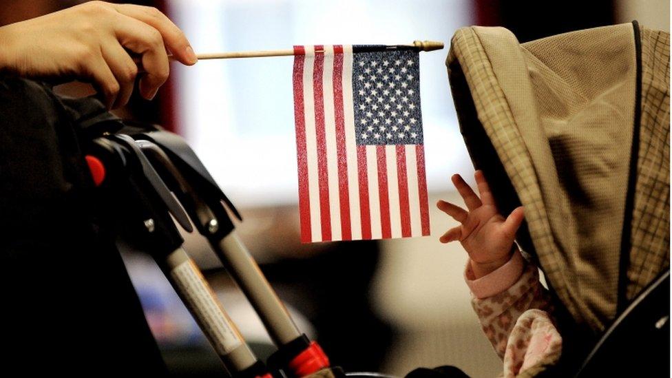 A baby reaches for an American flag held by her mother during naturalization ceremony at a federal building in New York, New York