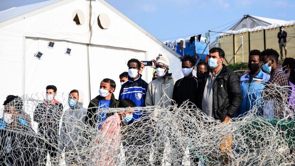 Migrants stand behind a fence at Karatepe refugee camp on Lesbos island, Greece, 29 March 2021