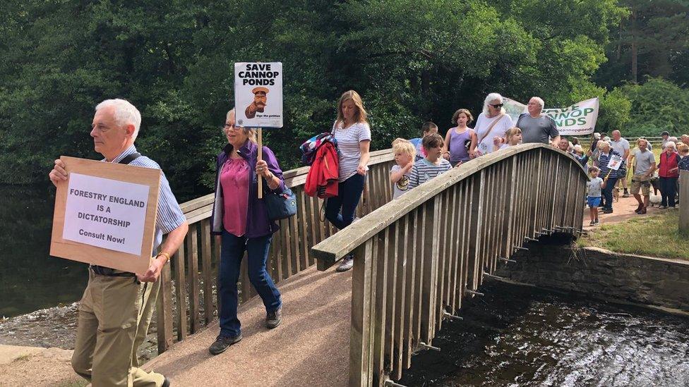 Save Our Ponds Campaign members marching over a bridge at Cannop Ponds holding placards