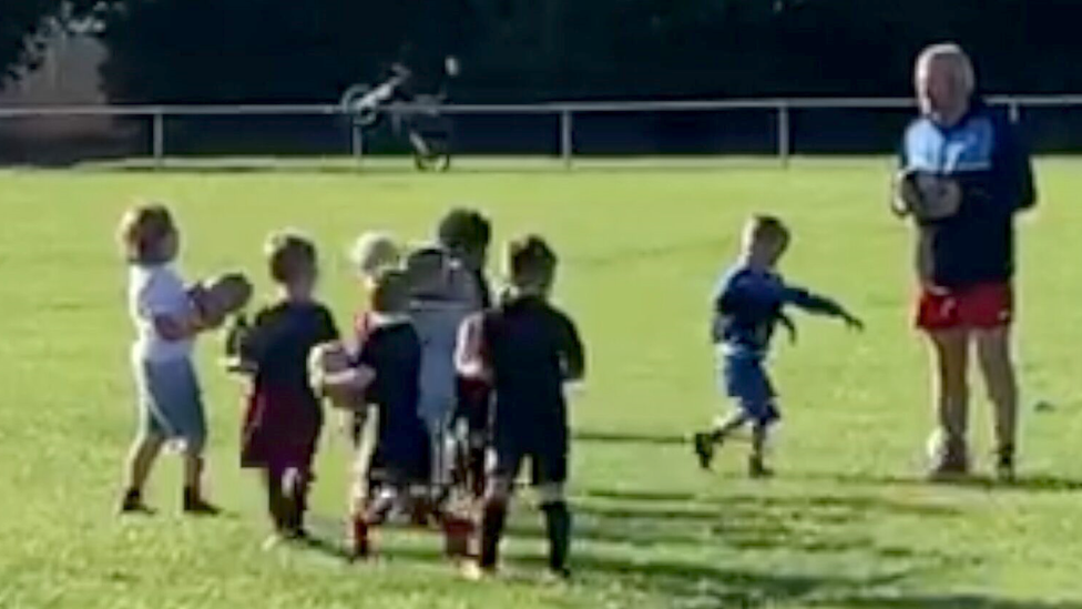 Young children at rugby training, with a motorbike doing a wheelie in the background