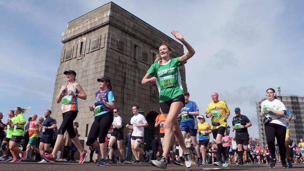 Woman in green Macmillan cancer support shirt waves to someone off camera as she takes part in the run