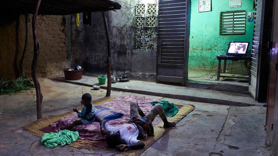 Two displaced children lie down to watch the television in the court of a house in Segou on September 30, 2019.