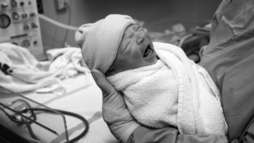 A baby boy is held by a midwife after being born in an NHS maternity unit, in Manchester, England