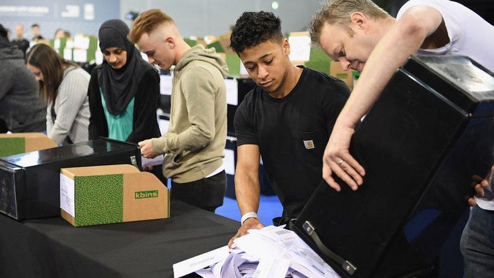 volunteers tipping ballot papers out of box at local election count