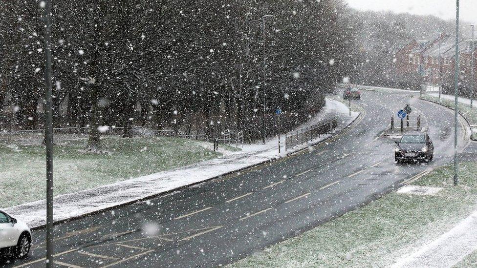 Heavy snow falling over a road with cars driving through