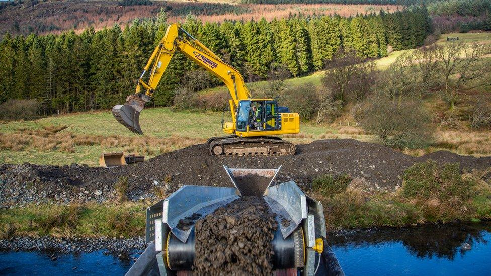 A shot of a digger transferring debris via a belt from one side of the river to the other