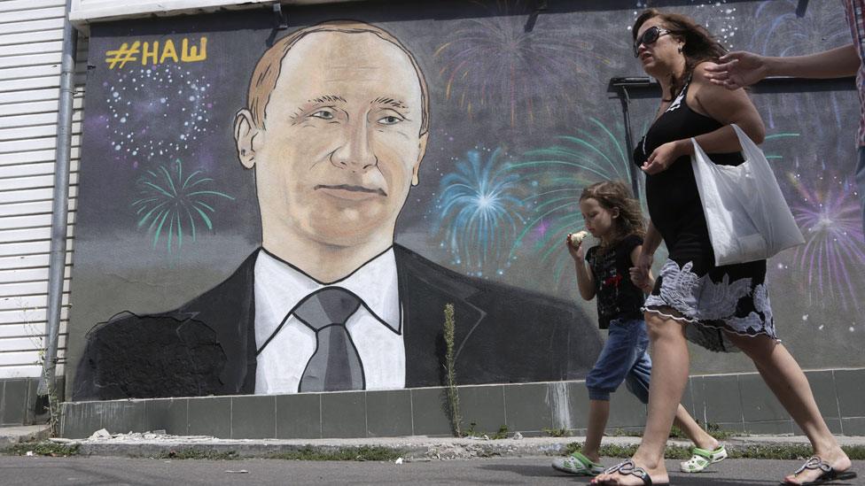 People walk past a graffito depicting Russia's President Vladimir Putin in the Crimean city of Simferopol o