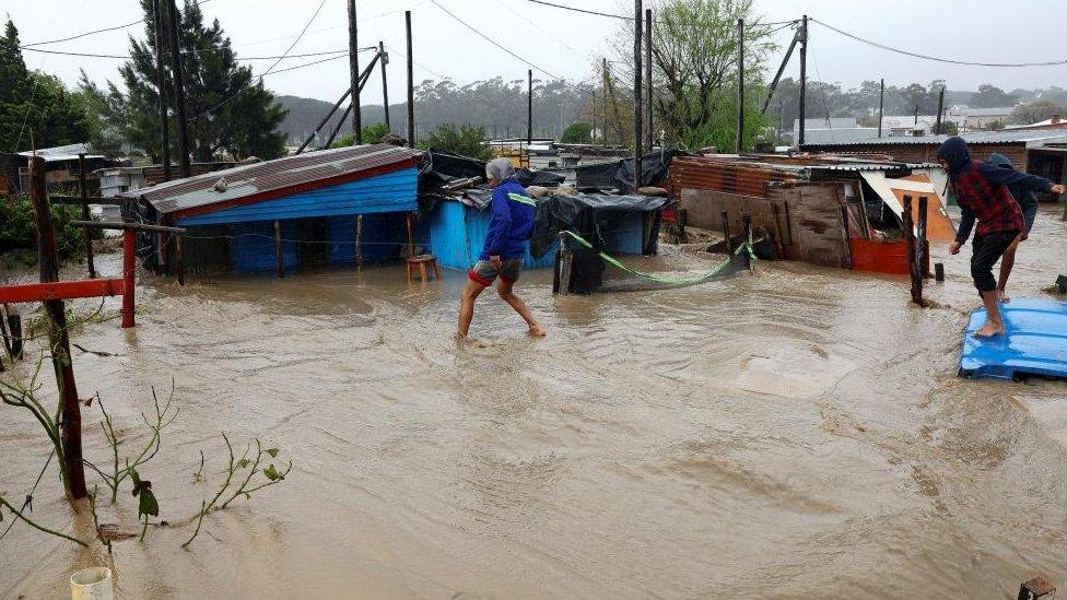 People walk next to the houses buried under mud following heavy rains in Sir Lowry's Pass Village, Western Cape, South Africa, September 25, 2023