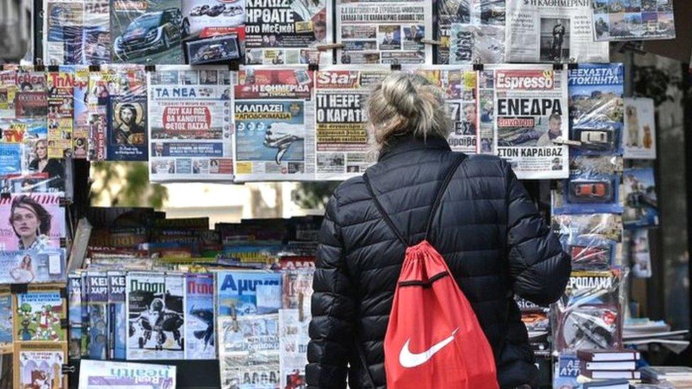 A woman reads newspaper's headlines referring to the killing of a Greek journalist in Athens on April 10, 2021.