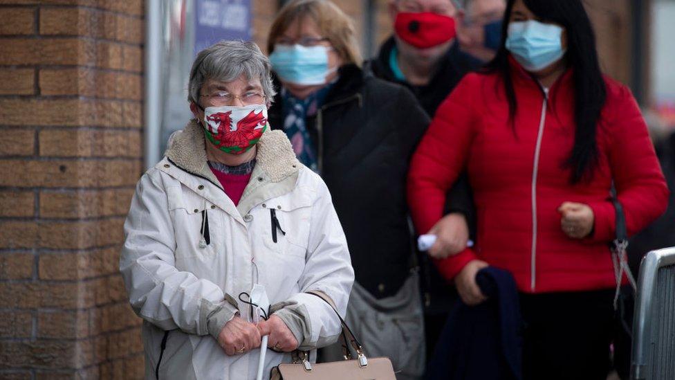 A woman wearing a Welsh flag face mask stands in a queue for vaccine