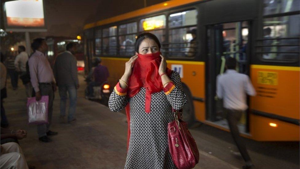 an Indian woman covers her face from pollution as she waits at a bus station in New Delhi, India.