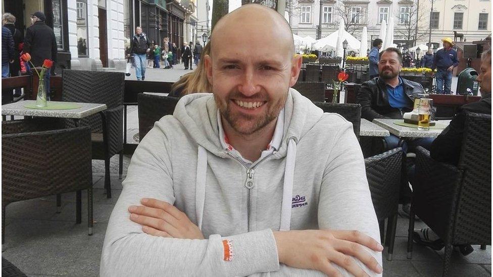 A bald man in a hoody sitting outside of a pub. He looks young.