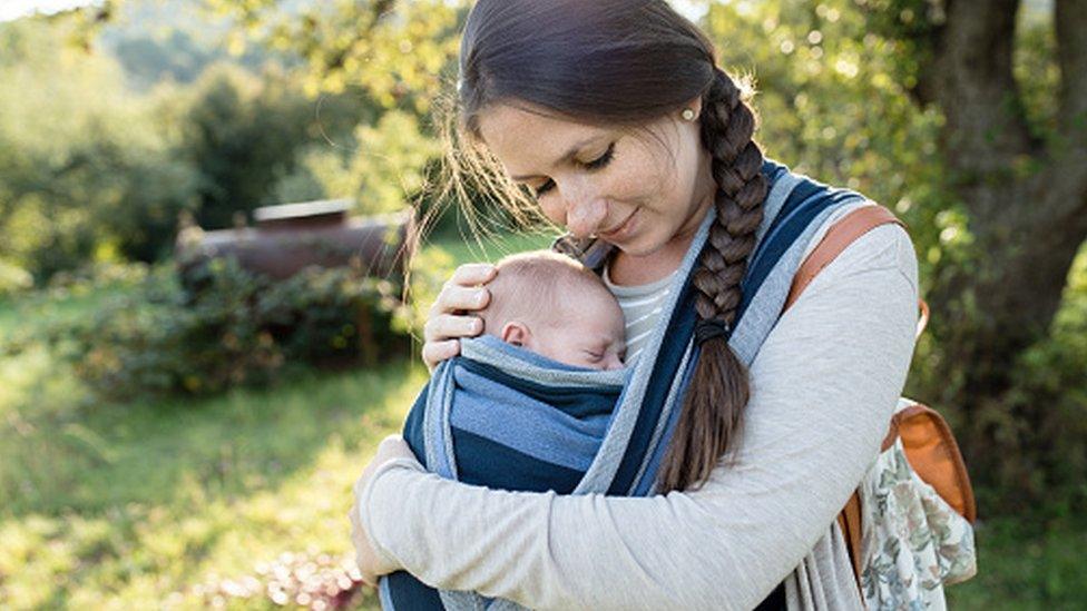 Young mum outside carrying her baby on her front