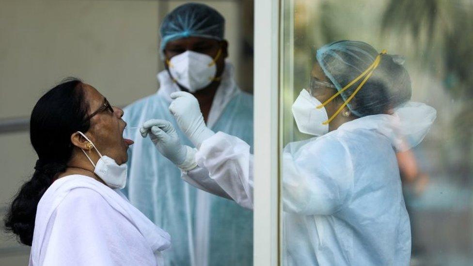 A healthcare worker in personal protective equipment (PPE) collects a swab sample from a woman during a testing campaign for the coronavirus disease (COVID-19), in Navi Mumbai, India