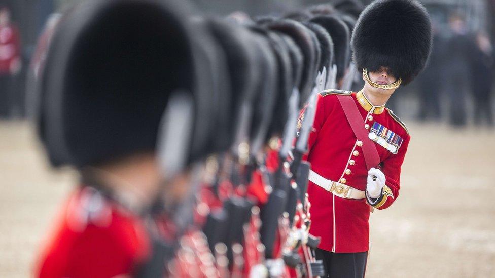 An officer of the Grenadier Guards leans out of a file of Guardsmen