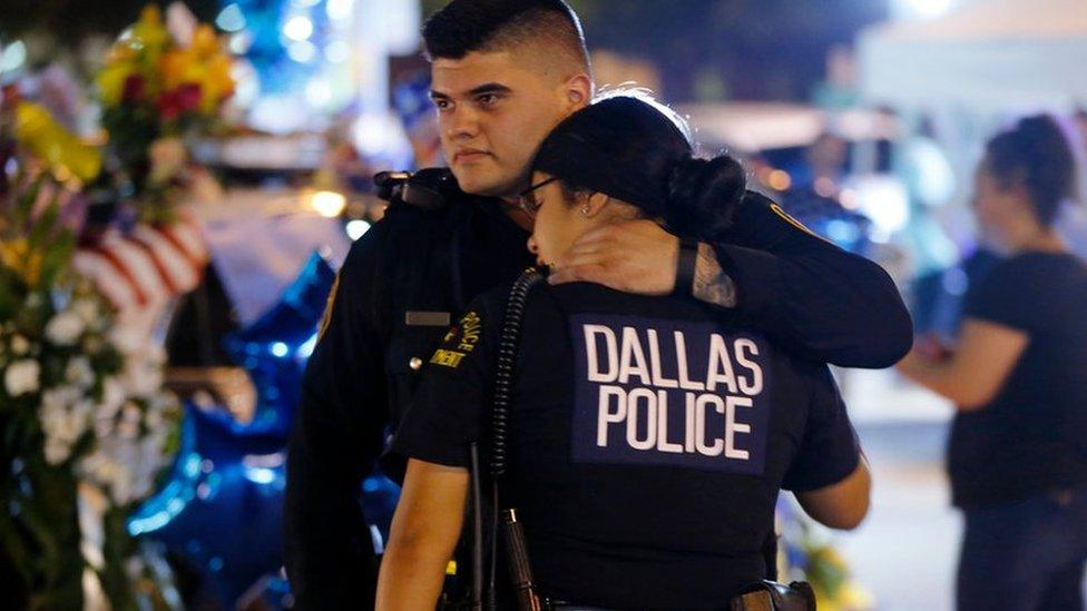 Dallas police officers comfort each other in Dallas in front of police cars decorated as a public memorial in front of police headquarters, in honour of Dallas police who were killed, on 8 July