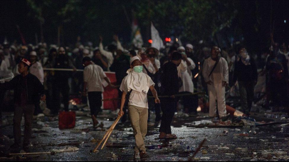 Protesters carrying sticks and wearing masks challenge police at a rally that turned violent on 4 November 2016 in Jakarta, Indonesia.