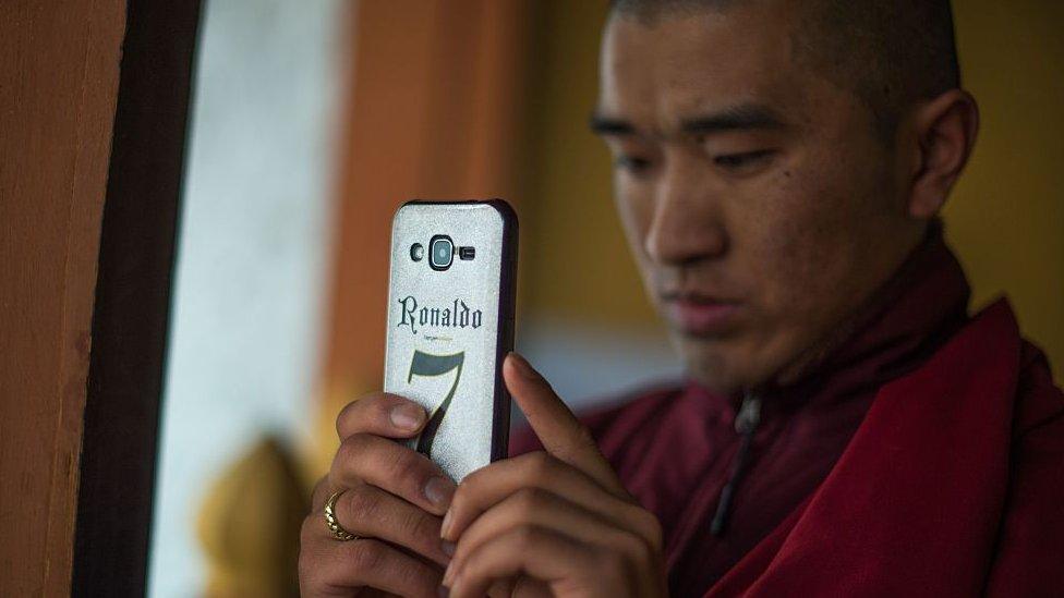 A Bhutanese Buddhist monk uses his mobile phone to take a photograph