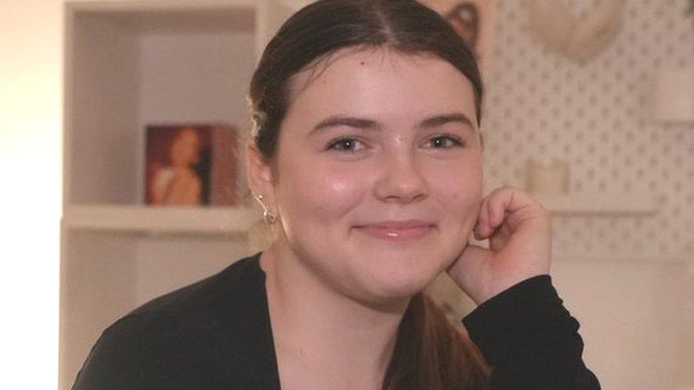 Martha, with her hair tied up and wearing a black top, smiles and looks into the camera