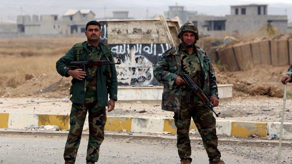Kurdish peshmerga forces stand in the street after Yazidi people loot houses in the town of Sinjar, Iraq