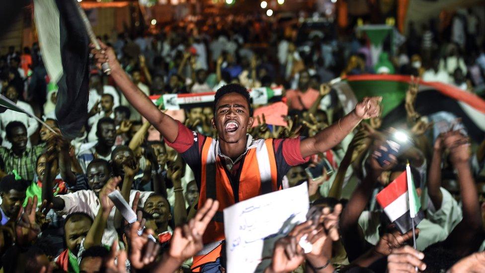 Sudanese protesters wave flags and flash victory signs as they gather for a sit-in outside the military headquarters in Khartoum on May 19, 2019. - Talks between Sudan's ruling military council and protesters are set to resume, army rulers announced, as Islamic movements rallied for the inclusion of sharia in the country's roadmap. (