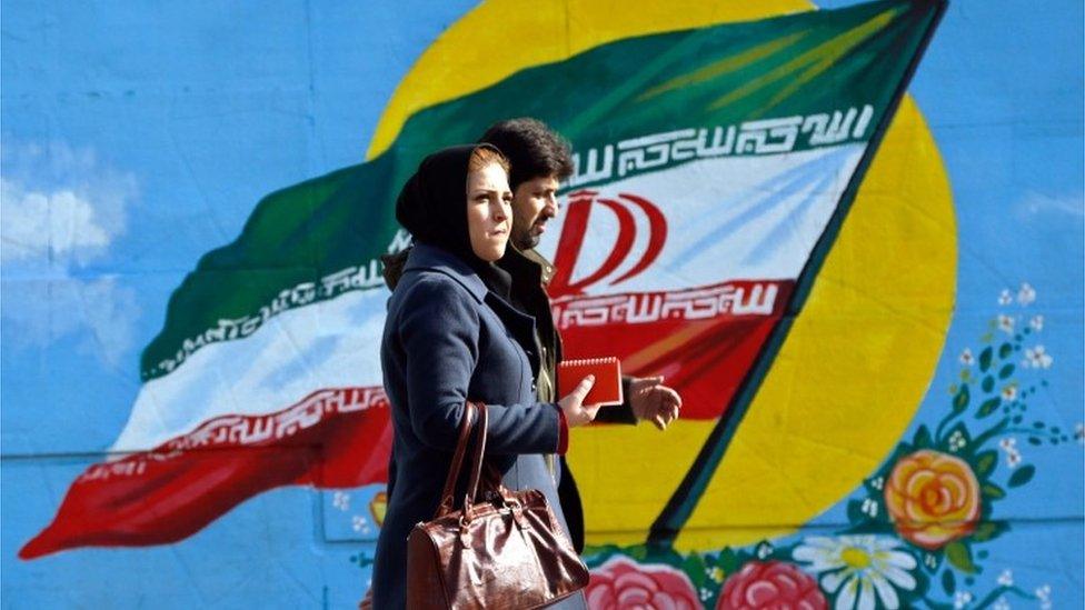 Man and woman walk past a mural of the Iranian flag in Tehran (file photo)