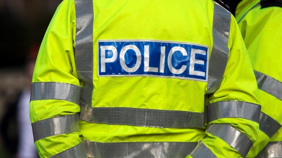 The back of a police officer wearing a reflective neon police jacket.