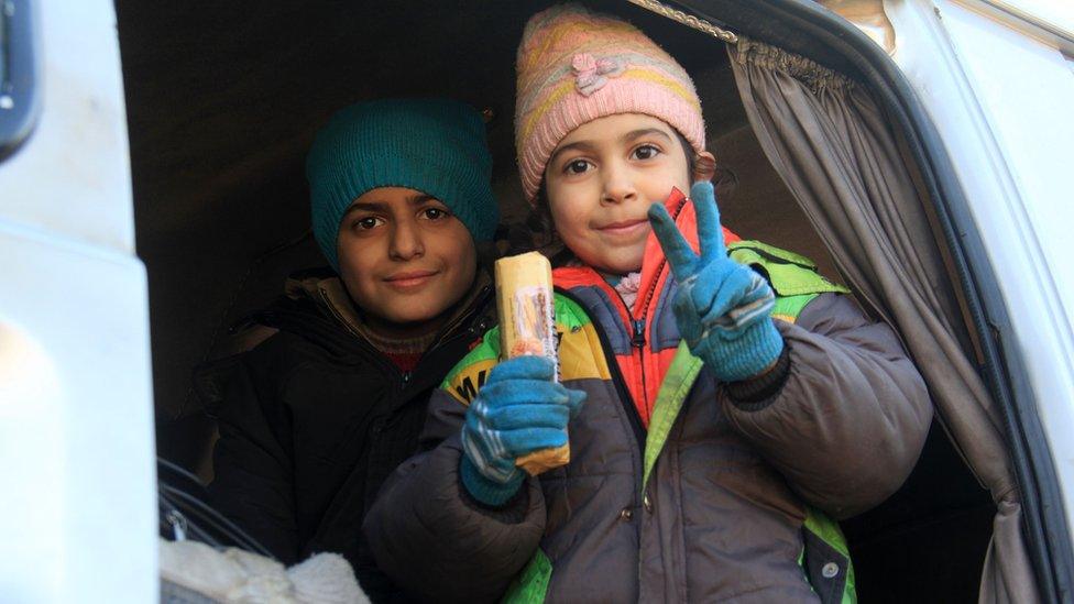 A Syrian child gives a peace sign from the door of a vehicle