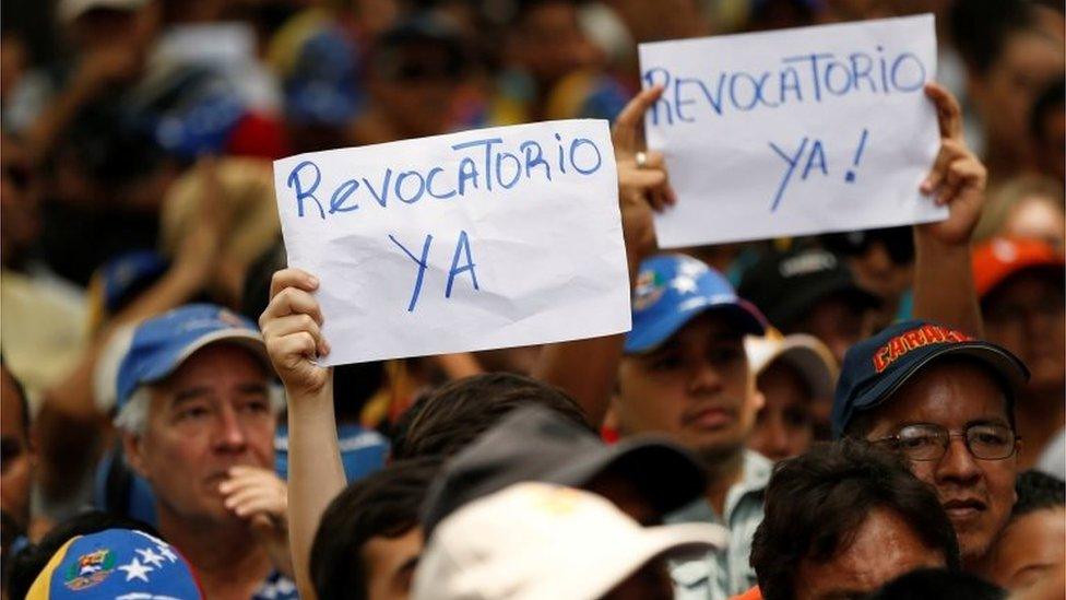 Opposition supporters hold signs that read, "Recall now" during a rally to demand a referendum to remove President Nicolas Maduro in Caracas, Venezuela, May 25, 2016