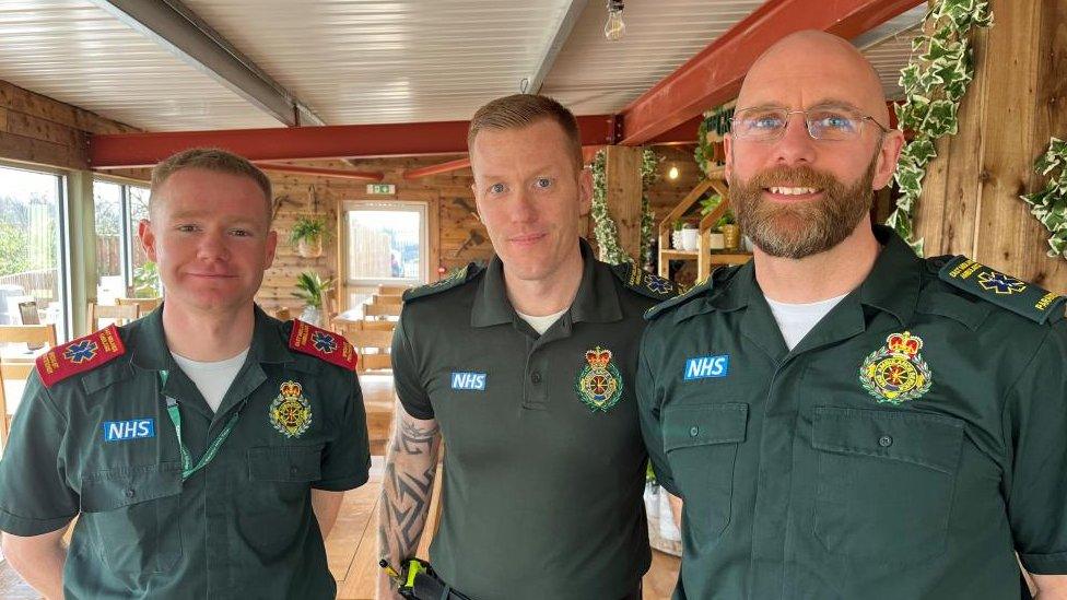 Ian, Matt and Scott in green uniforms in a garden centre. Matt has a beard.