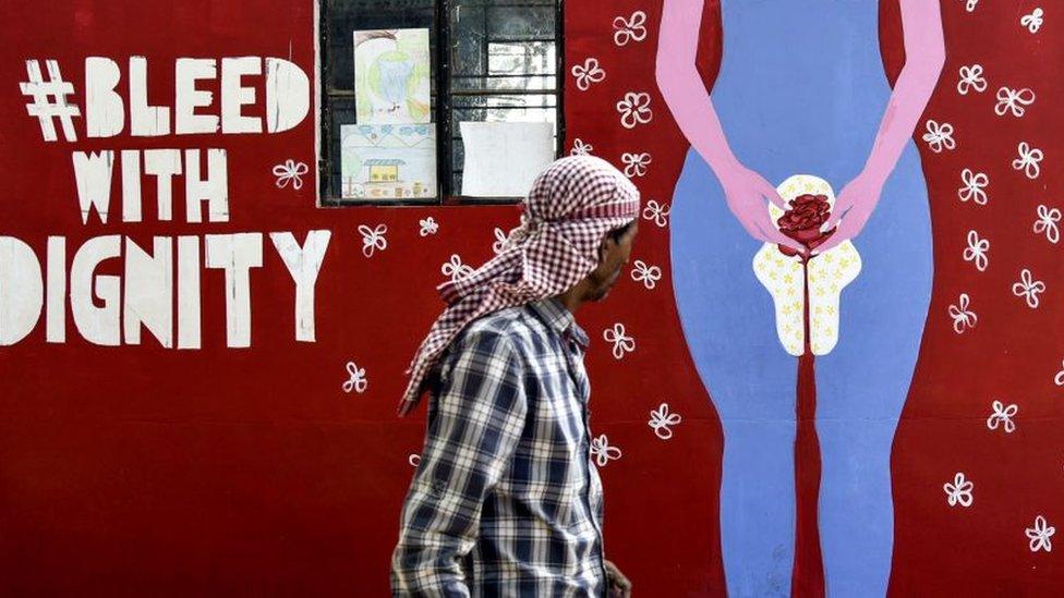 An Indian man looks on as he walks along a wall painting about menstruation in Guwahati on May 28, 2019