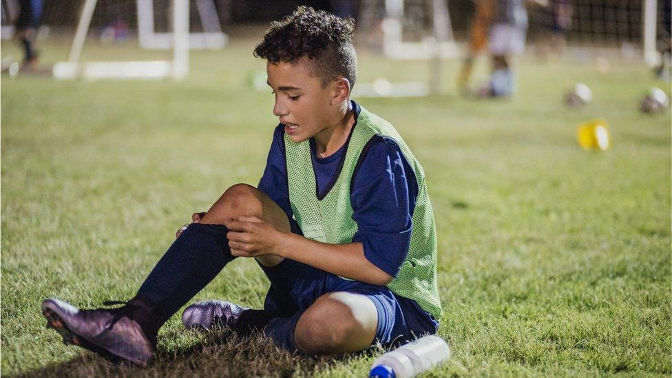 A young football player sitting on the ground looking at his leg