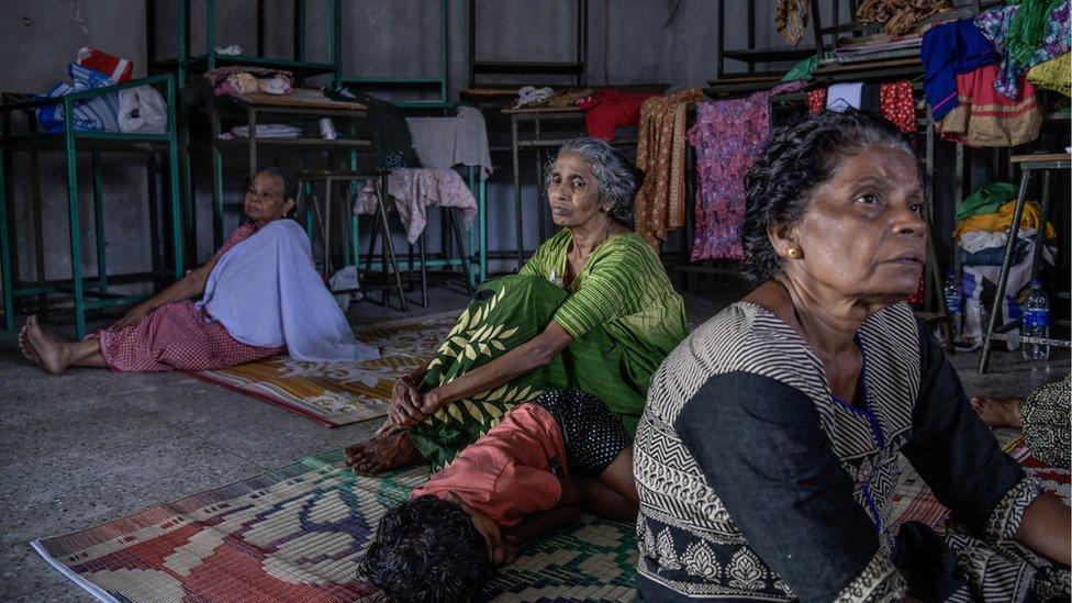 Three woman and a child sit on rugs in a makeshift shelter