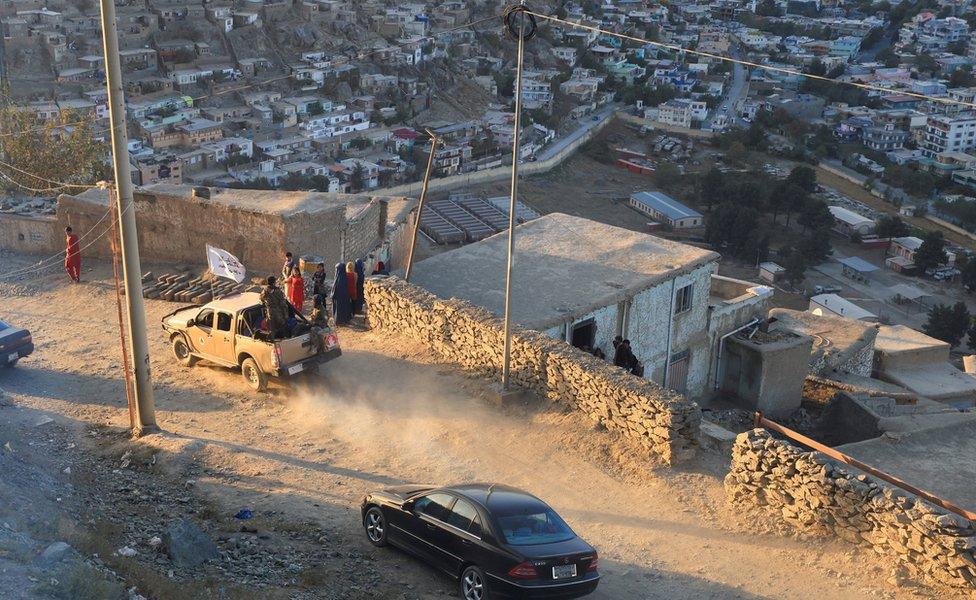 Taliban fighters riding their car are pictured through a window as they drive past a family at Tv mountain in Kabul,