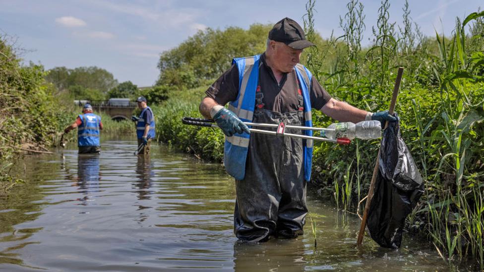 Volunteers clean up a river next to riverbank grass