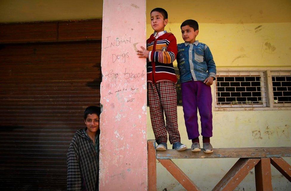 Children stand next to anti-India graffiti on the school wall