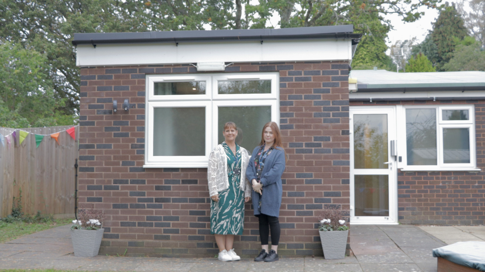 two women stand outside a bungalow