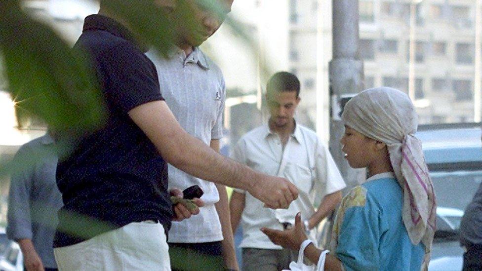 Men give money to a young beggar in Cairo (file photo)