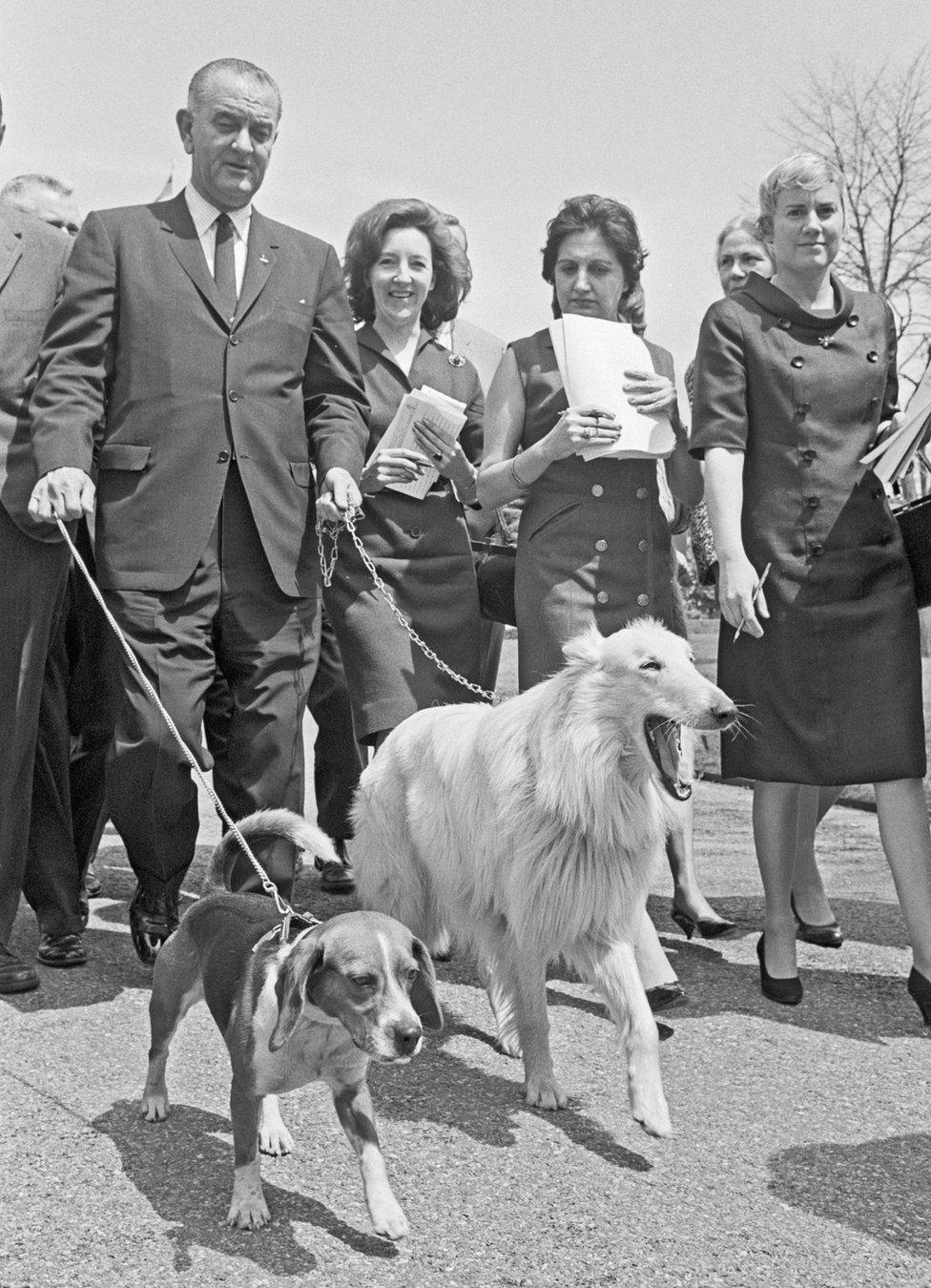 President Johnson walks his dogs whilst surrounded by journalists