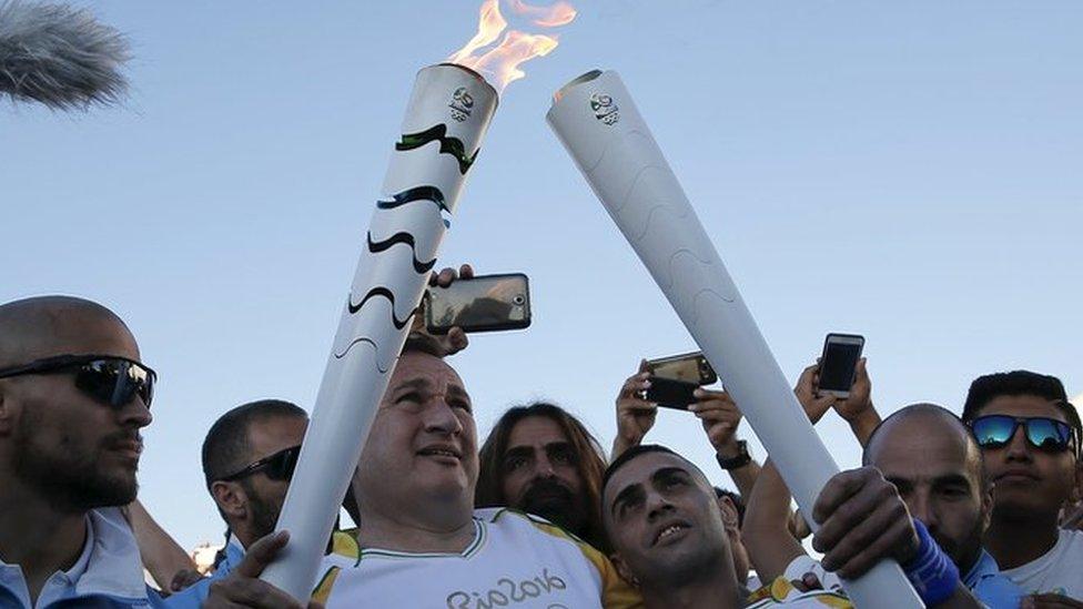 President of the Hellenic Olympic Committee Spiros Kapralos (2nd L) hands over the Olympic Flame to Syrian refugee Ibrahim al-Hussein (2nd R), an amputee swimmer, during the Olympic Flame torch relay at the Eleonas refugee camp in Athens, Greece, April 26, 2016