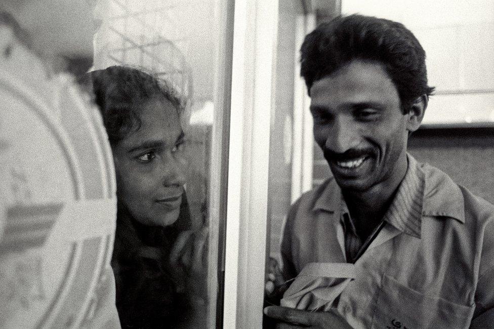 A woman looks at her husband through a window at Dhaka airport