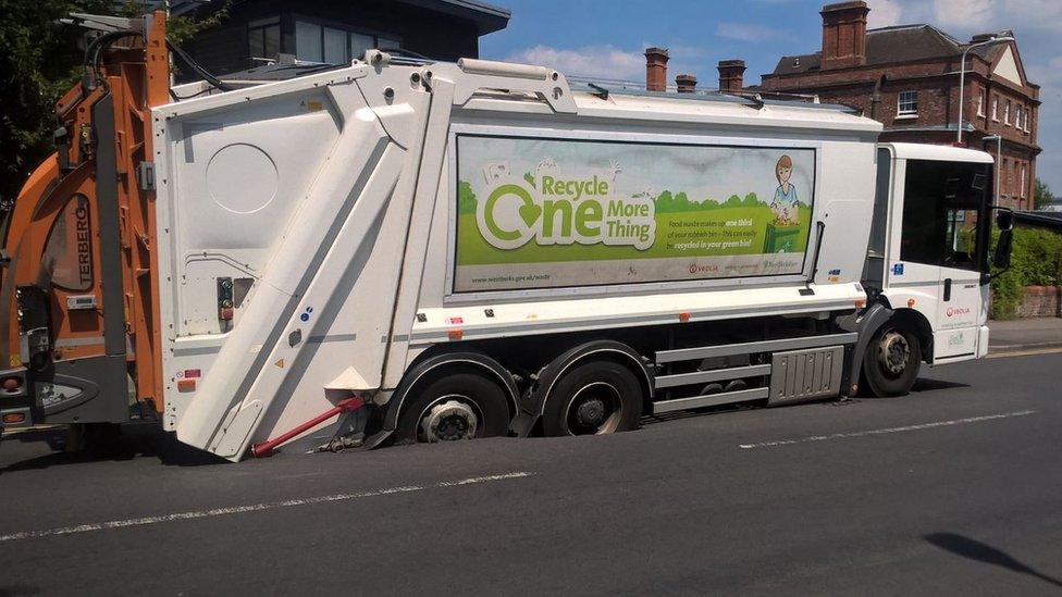 Bin lorry sinks in road